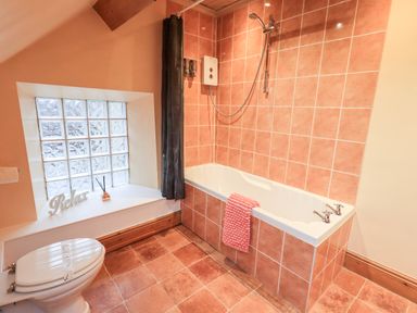 A bathroom with a bathtub shower toilet and a window with decorative items at Granary Nook in Windermere