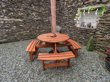 A round wooden picnic table with attached benches inside a stone walled courtyard at Granary Nook in Windermere