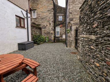 A stone courtyard with a wooden bench table and gravel ground at Granary Nook in Windermere