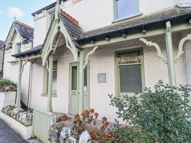Front entrance of a house with a wooden porch and green door and window frames at Greta Mill in Keswick