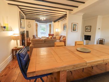A dining room with a wooden table and chairs leading into a living room with sofas a television and window seats at Greta Mill in Keswick