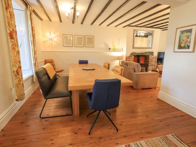 A dining area with a wooden table and mixed chairs next to a sitting area with sofas and a fireplace at Greta Mill in Keswick