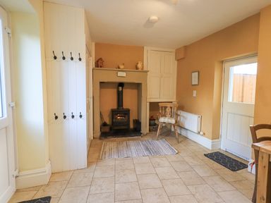 A room with a wood burning stove in a fireplace a wooden chair a door and tiled floor at Greta Mill in Keswick