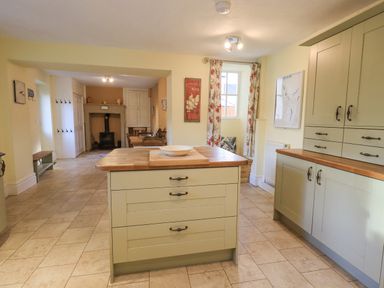 A kitchen with an island and built-in cabinets leading to a dining area with a wood stove at Greta Mill in Keswick