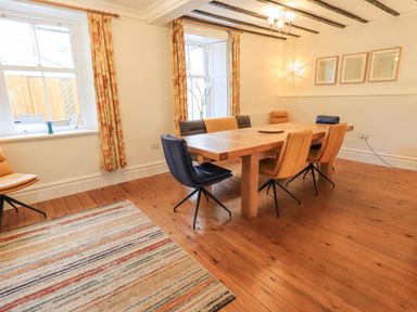 A dining room with a wooden table and mixed color chairs next to windows with floral curtains at Greta Mill in Keswick