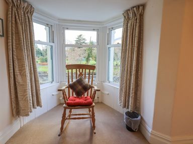 A wooden rocking chair with cushions in front of bay windows with curtains at Greta Mill in Keswick