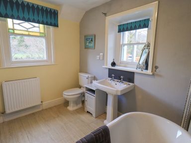 A bathroom with a toilet a pedestal sink a bathtub and two windows with blue valances at Greta Mill in Keswick