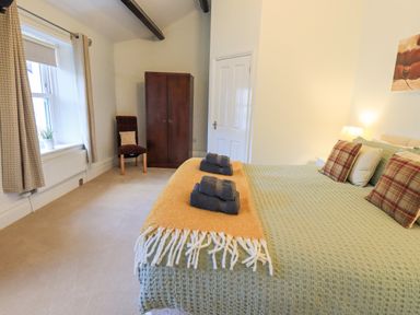 A bedroom with a double bed with pillows and folded towels and a wardrobe and chair near a window at Greta Mill in Keswick
