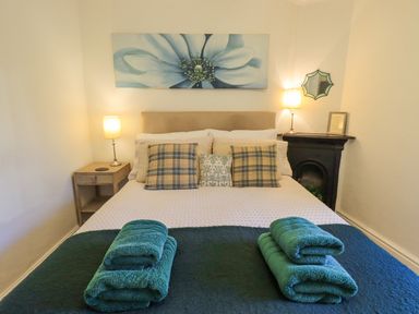 A bedroom with a bed featuring pillows and folded towels two bedside tables with lamps and a floral painting above the bed at Greta Mill in Keswick