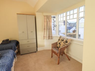 A corner of a bedroom with a wardrobe bed with blue covers a wicker chair with cushions and windows at Greta Mill in Keswick