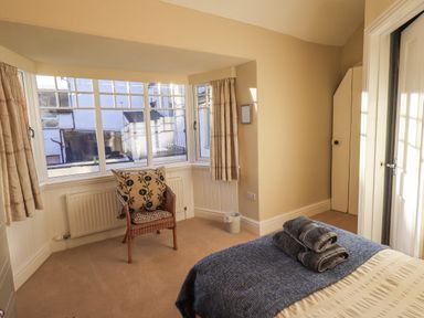 A bedroom with a bed with folded towels a wicker chair and large windows at Greta Mill in Keswick