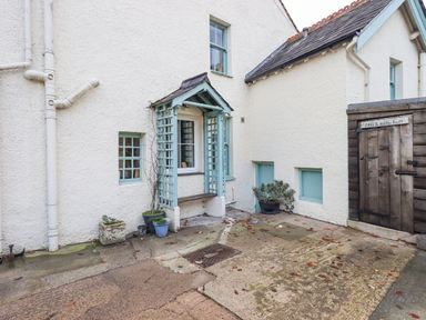 An exterior view of a white house with blue window frames and a small blue covered porch with a bench and potted plants outside at Greta Mill in Keswick