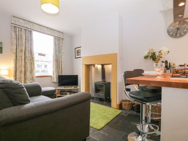 A living area with a sofa television and wood stove next to a kitchen counter with bar stools at Banks Place in Keswick
