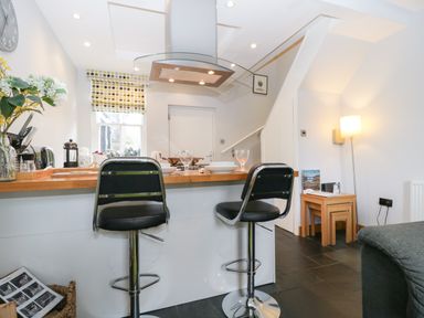 A kitchen area with two black bar stools at a wooden counter and a lamp next to nested wooden tables at Banks Place in Keswick
