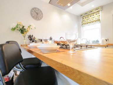A kitchen with a wooden countertop stools bowls glasses a gas stove and a window with patterned blinds at Banks Place in Keswick