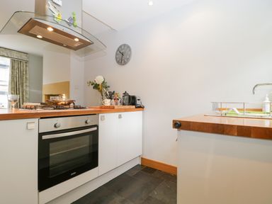 A kitchen with an oven stove a clock on the wall and utensils on the counter at Banks Place in Keswick