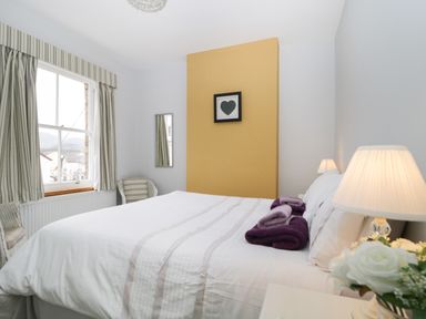 A bedroom with a bed folded towels a window with curtains a bedside lamp and a framed heart picture on a yellow wall at Banks Place in Keswick