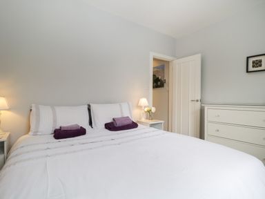 A bedroom with a double bed white bedding purple towels bedside tables lamps and a white dresser at Banks Place in Keswick