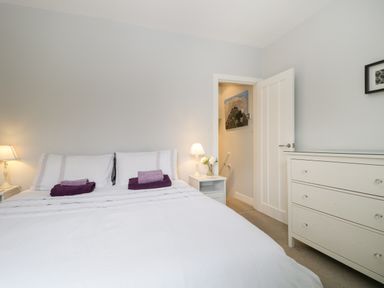 A bedroom with a double bed with white bedding and purple towels a white dresser and bedside tables with lamps at Banks Place in Keswick
