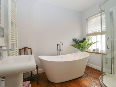 A bathroom with a freestanding bathtub a shower enclosure a sink a wooden floor and a window with blinds at Banks Place in Keswick
