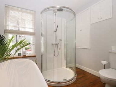 A bathroom with a curved glass shower enclosure a toilet a bathtub a window with blinds and a plant at Banks Place in Keswick