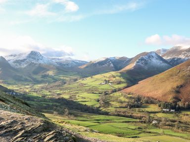 A valley with green fields and scattered trees surrounded by mountains with some snow at Tree Tops View in Bowness-On-Windermere