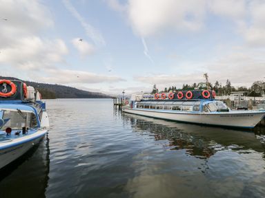 A dock with two passenger boats on a lake with hills and trees in the background at Tree Tops View in Bowness-On-Windermere