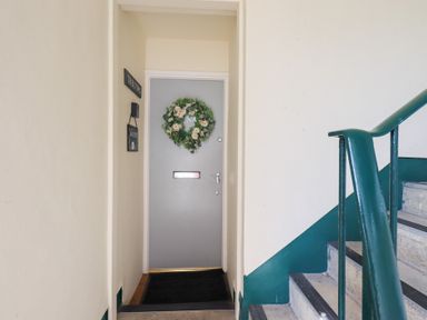 An indoor stairway with green railings near a grey door decorated with a floral wreath at Tree Tops View in Bowness-On-Windermere