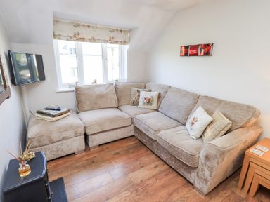 A living room with a beige sectional sofa and cushions next to a window and a wall-mounted TV at Tree Tops View in Bowness-On-Windermere