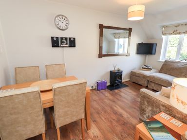 A living room with a dining table and chairs a sofa a TV mounted on the wall a wall clock and a mirror at Tree Tops View in Bowness-On-Windermere