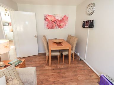 A dining area with a wooden table four chairs floral painting wall clock and a stereo at Tree Tops View in Bowness-On-Windermere