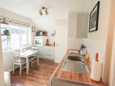 A kitchen with a dining table and two chairs a sink oven microwave and window at Tree Tops View in Bowness-On-Windermere