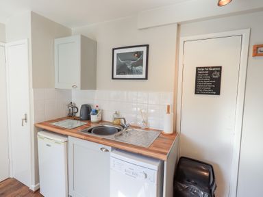 A kitchen area with a sink, countertop, cabinets, a small fridge, kettle, and a dishwasher at Tree Tops View in Bowness-On-Windermere