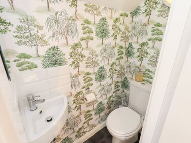 A small bathroom with a white toilet and corner sink with tree patterned wallpaper at Tree Tops View in Bowness-On-Windermere