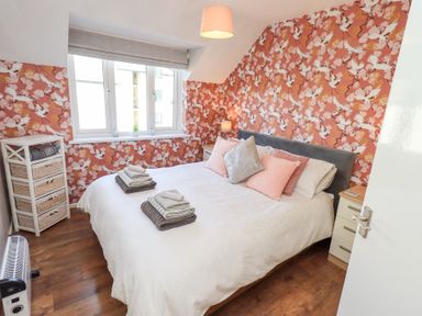 A bedroom with a double bed with folded towels and cushions next to a window with floral wallpaper at Tree Tops View in Bowness-On-Windermere
