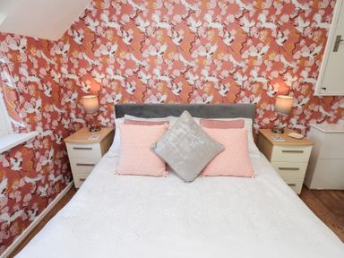 A bedroom with a bed and pillows between two bedside tables with lamps and decorative wallpaper at Tree Tops View in Bowness-On-Windermere