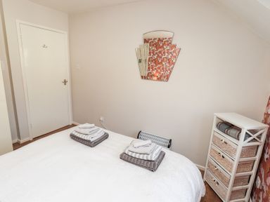 A bedroom with a bed with folded towels a wall mirror a chest of drawers and a closed door at Tree Tops View in Bowness-On-Windermere