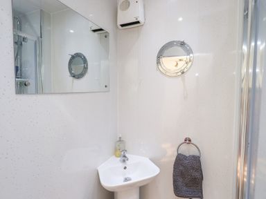 A bathroom with a corner sink a mirror a small round window a hand towel on a ring and a wall-mounted fan at Tree Tops View in Bowness-On-Windermere