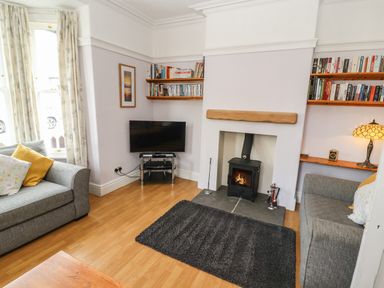 A living room with two grey sofas a wood burning stove television and bookshelves at Pelham House in Keswick
