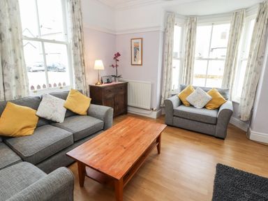 A sitting room with grey sofas yellow and floral cushions a wooden coffee table and a wooden sideboard with a lamp at Pelham House in Keswick