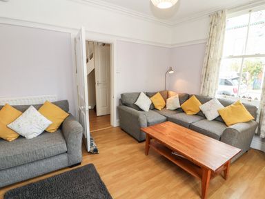 A living room with two gray sofas with yellow and floral cushions a wooden coffee table and a window with curtains at Pelham House in Keswick