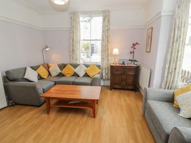A living room with gray sofas yellow and floral cushions a wooden coffee table and a wooden cabinet with a lamp and flower at Pelham House in Keswick