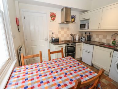 A kitchen with a checkered tablecloth on a wooden table and four chairs oven microwave and sink at Pelham House in Keswick