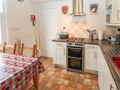 A kitchen with a stove toaster microwave and wooden chairs by a table with a checkered tablecloth at Pelham House Keswick