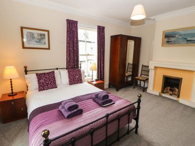 A bedroom with a double bed with purple bedding and towels near a window with curtains beside wooden furniture and a fireplace at Pelham House in Keswick