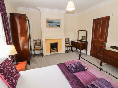 A bedroom with a bed, bedside table, wardrobe, fireplace, chairs, dresser with mirror, and wooden door at Pelham House in Keswick