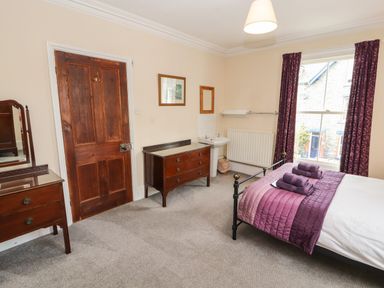 A bedroom with a bed, wooden door, two wooden dressers, a small sink, window with curtains at Pelham House in Keswick