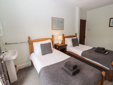 A bedroom with two single beds a wooden nightstand with a lamp a sink and towels at Pelham House in Keswick