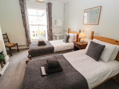 A bedroom with two single beds a window a chair and a bedside table with a lamp at Pelham House in Keswick