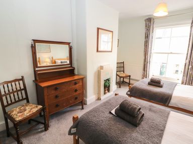 A bedroom with two single beds towels on beds wooden dresser with mirror two wooden chairs at Pelham House in Keswick